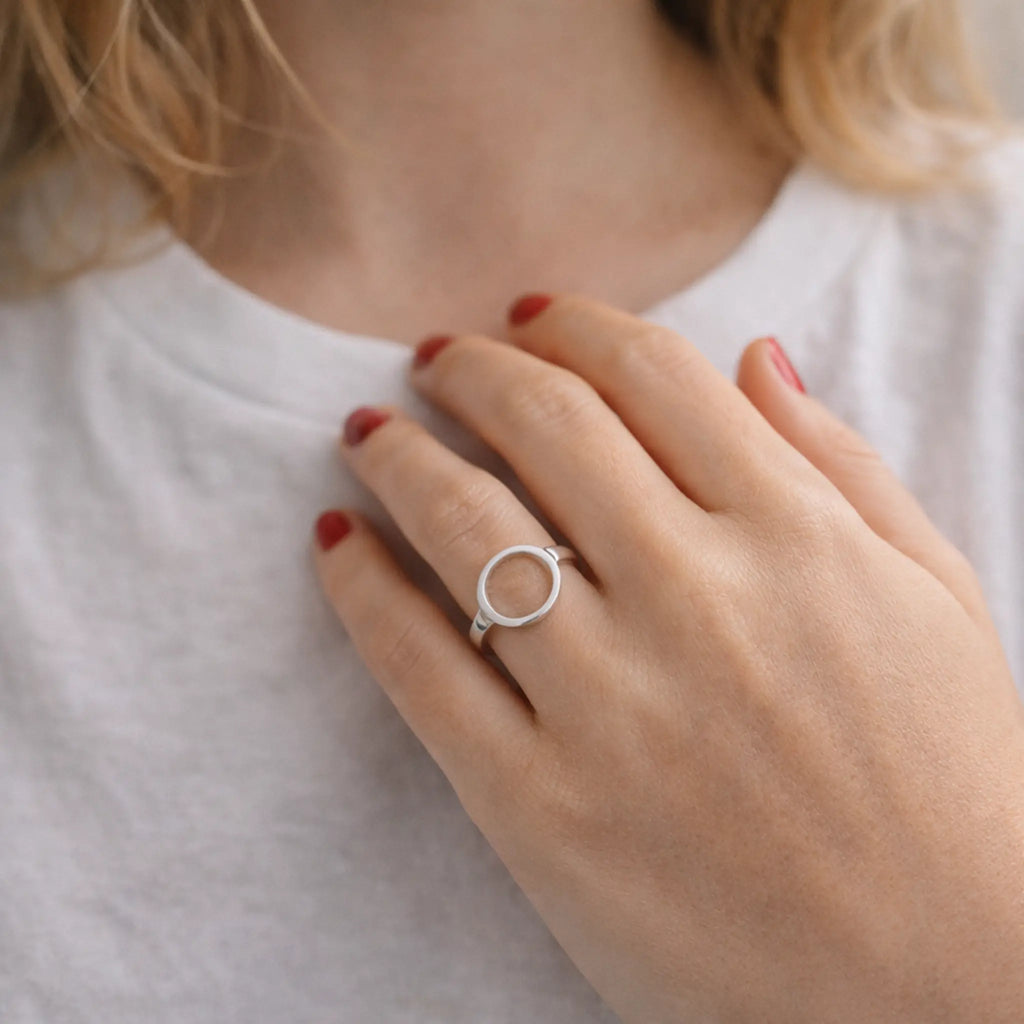 Minimalistischer Silberring im Kreis-Design an der Hand, rote Nägel, weißes T-Shirt – moderner Damenring im cleanen Look, Nahaufnahme.