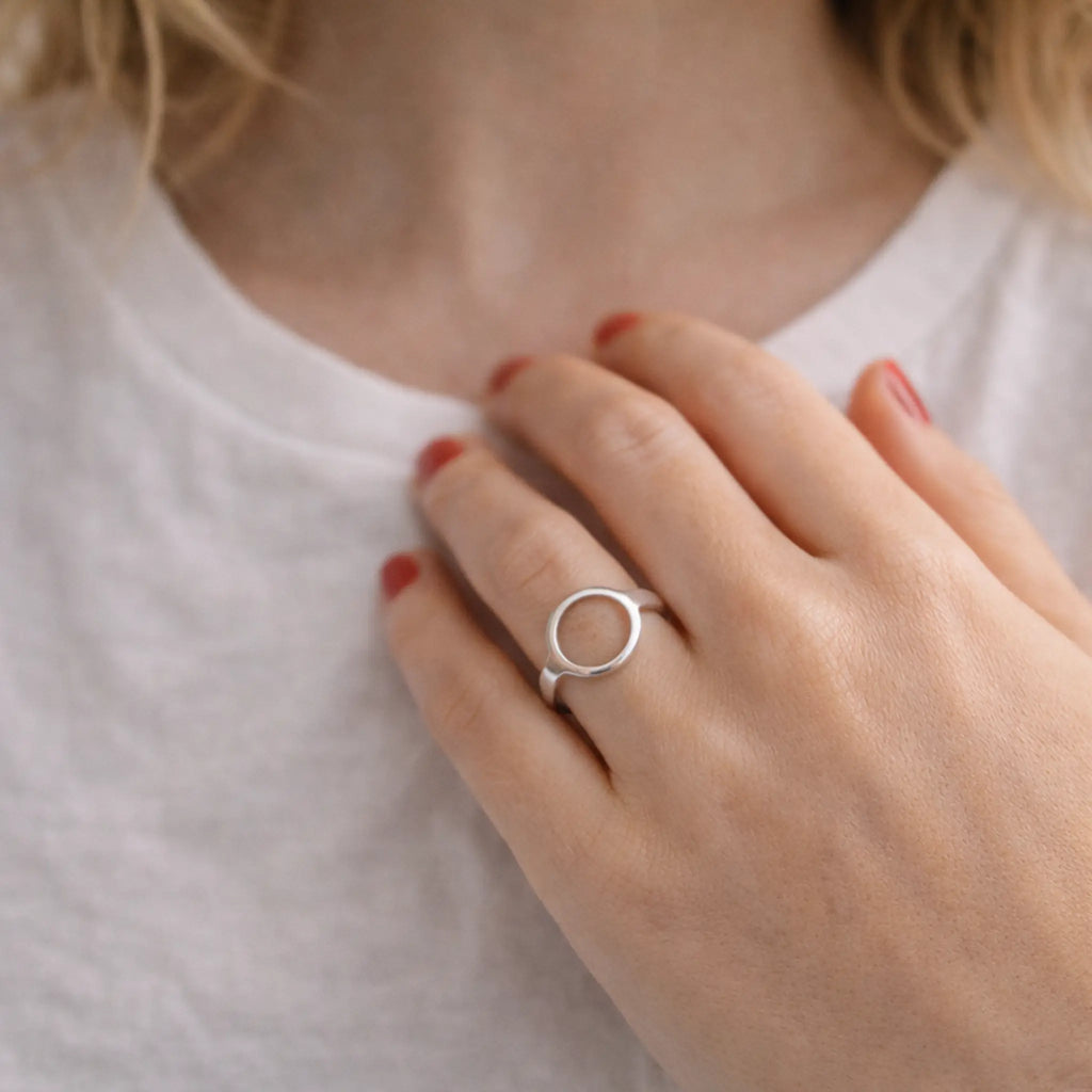 Nahaufnahme: Hand auf weißem Shirt mit schlichtem Silberring als Kreis – moderner Damenring, minimalistisch, rote Nägel, Lifestyle-Foto.