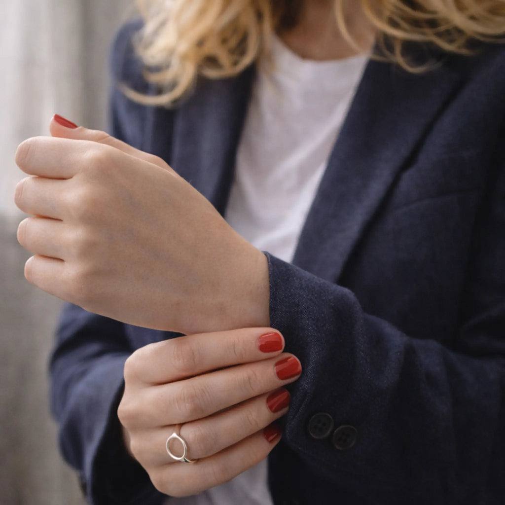 Frau im Blazer richtet den Ärmel, rote Nägel, minimalistischer Kreis-Silberring – eleganter Damenring fürs Business-Outfit.