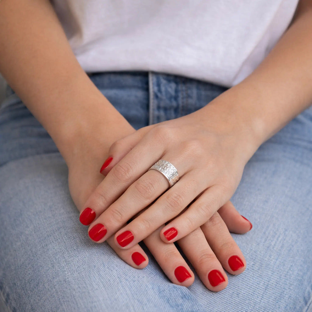 Massiver Silberring Damen strukturiert auf verschränkten Händen vor blauer Jeans.