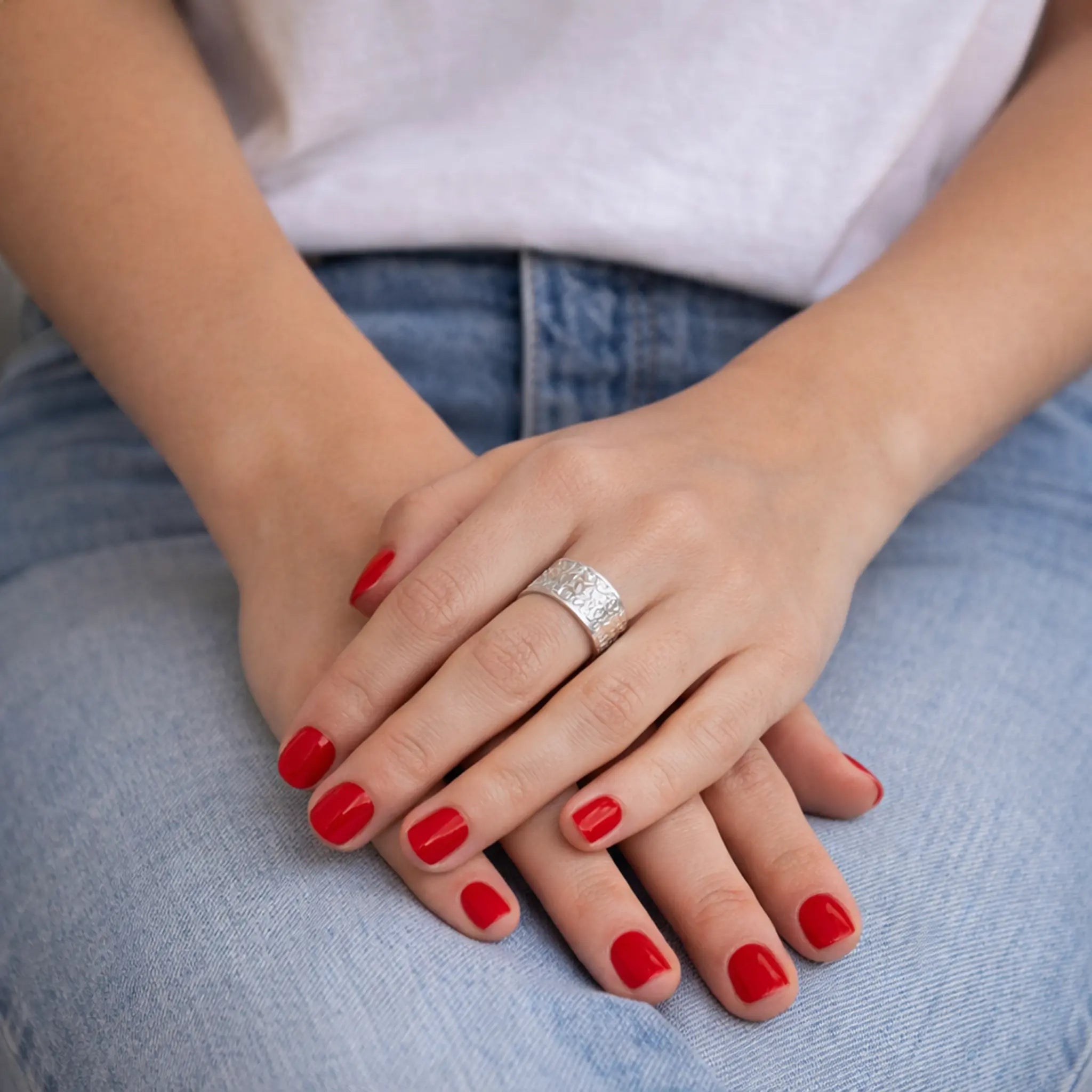 Massiver Silberring Damen strukturiert auf verschränkten Händen vor blauer Jeans.