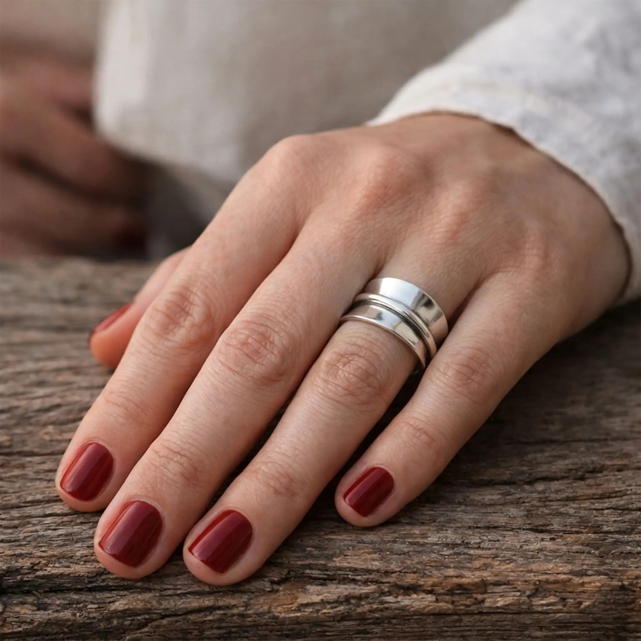Breiter Damenring aus 925 Sterling Silber, verstellbarer Silberring mit glänzender Oberfläche, Nahaufnahme einer Hand mit dunkelrotem Nagellack auf rustikalem Holz