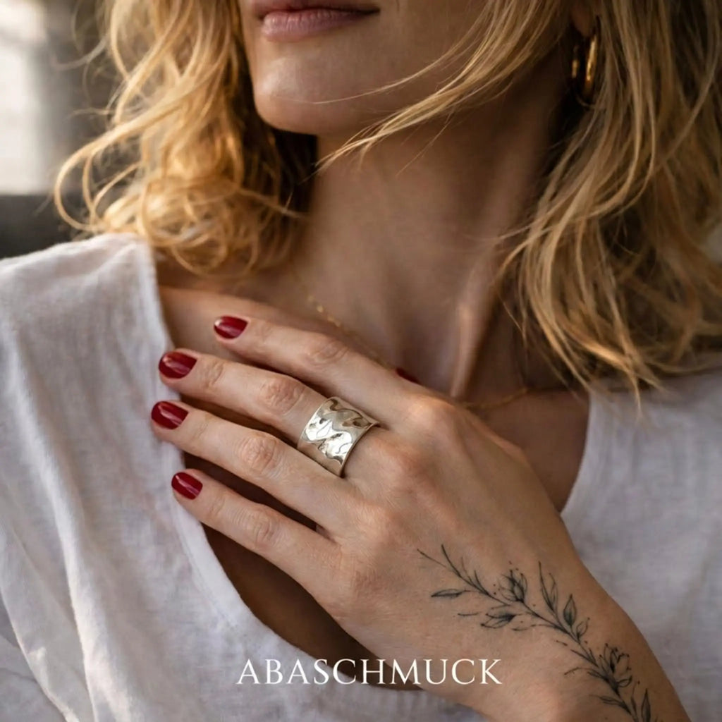 Eleganter breiter Silberring aus 925 Sterling Silber mit organischer Struktur, verstellbarer Damenring an der Hand einer blonden Frau mit rotem Nagellack und botanischem Tattoo im Lifestyle Foto