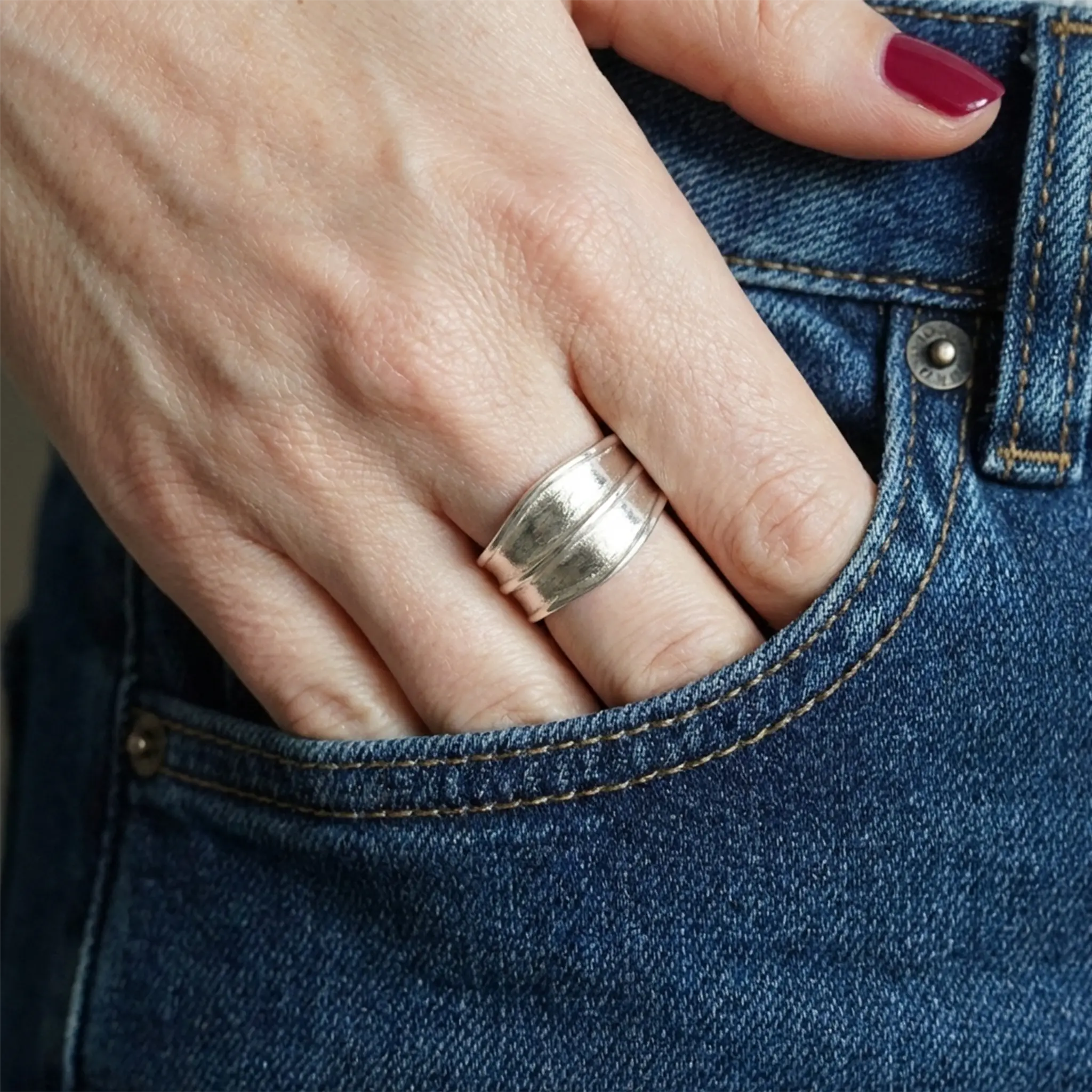Detailaufnahme: breiter Silberring am Finger, Hand in der Jeanstasche, bordeauxrote Nägel, Casual-Style.