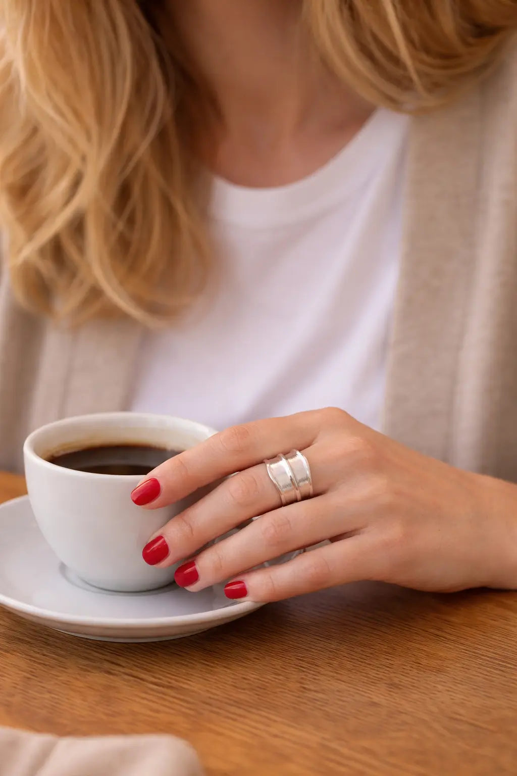 Nahaufnahme: Frau mit Lederjacke hält Tasse; breiter Silberring aus Silber am Finger, rote Nägel, urbaner Lifestyle-Look.