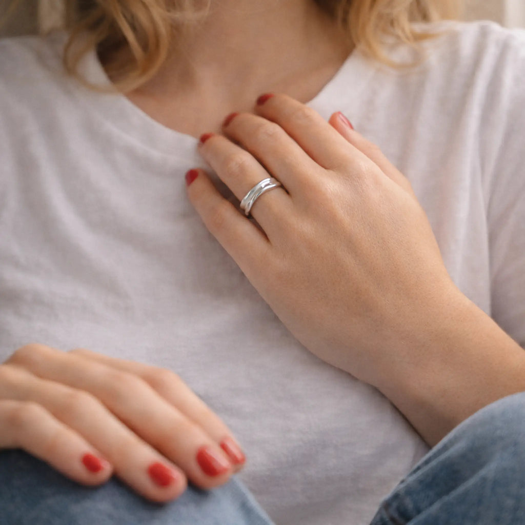 Lifestyle-Porträt: Frau in weißem T-Shirt und Jeans, Hand auf der Brust mit minimalistischer Silberring für Damen, rote Nägel, ruhiger Look.