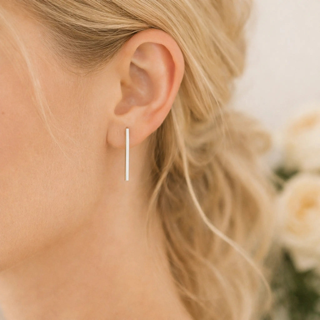 Minimalistische Silberohrringe 925 in Stabform, elegante Ohrhänger aus Sterling Silber am Ohr einer blonden Frau, moderner Damen Ohrschmuck in Nahaufnahme