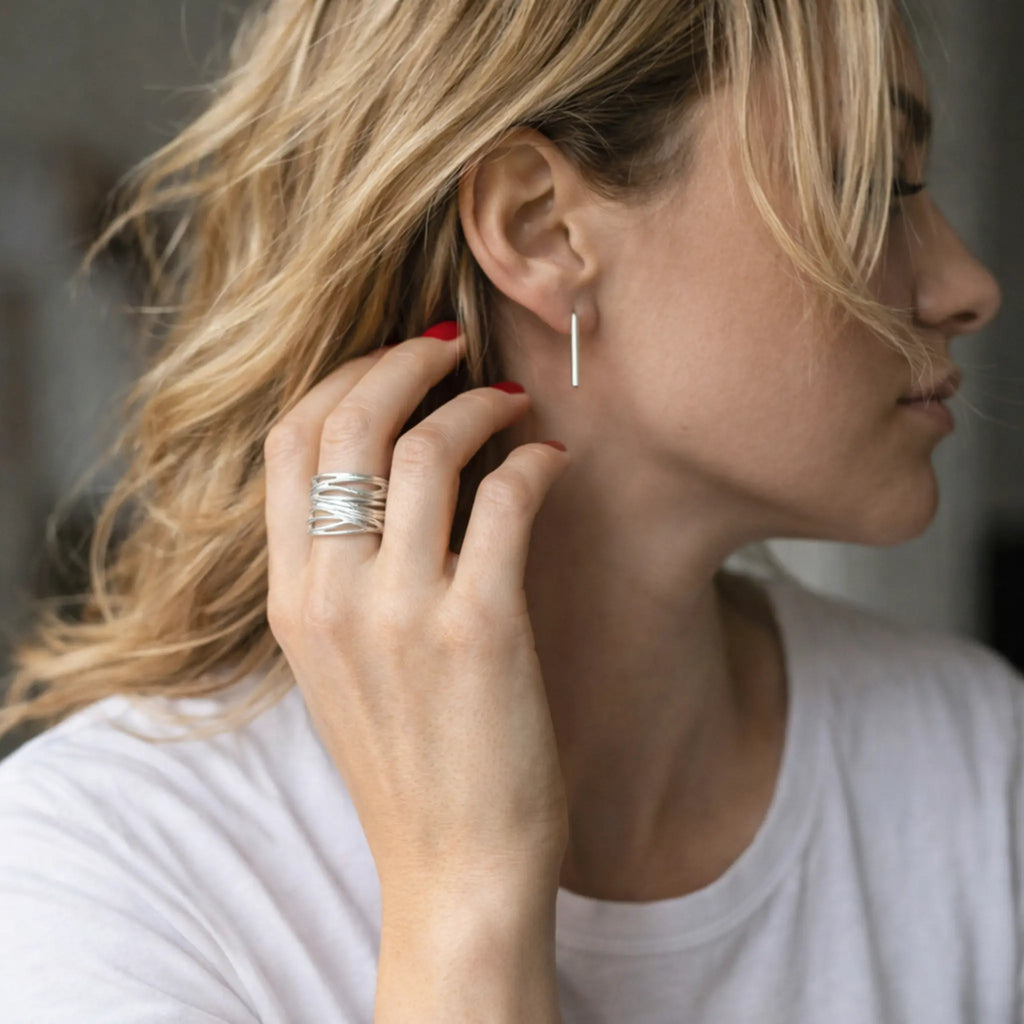 Feine Silberohrringe aus 925 Sterling Silber in modernem Stäbchen Design, eleganter Ohrschmuck an blonder Frau mit weißem Shirt und silbernem Ring