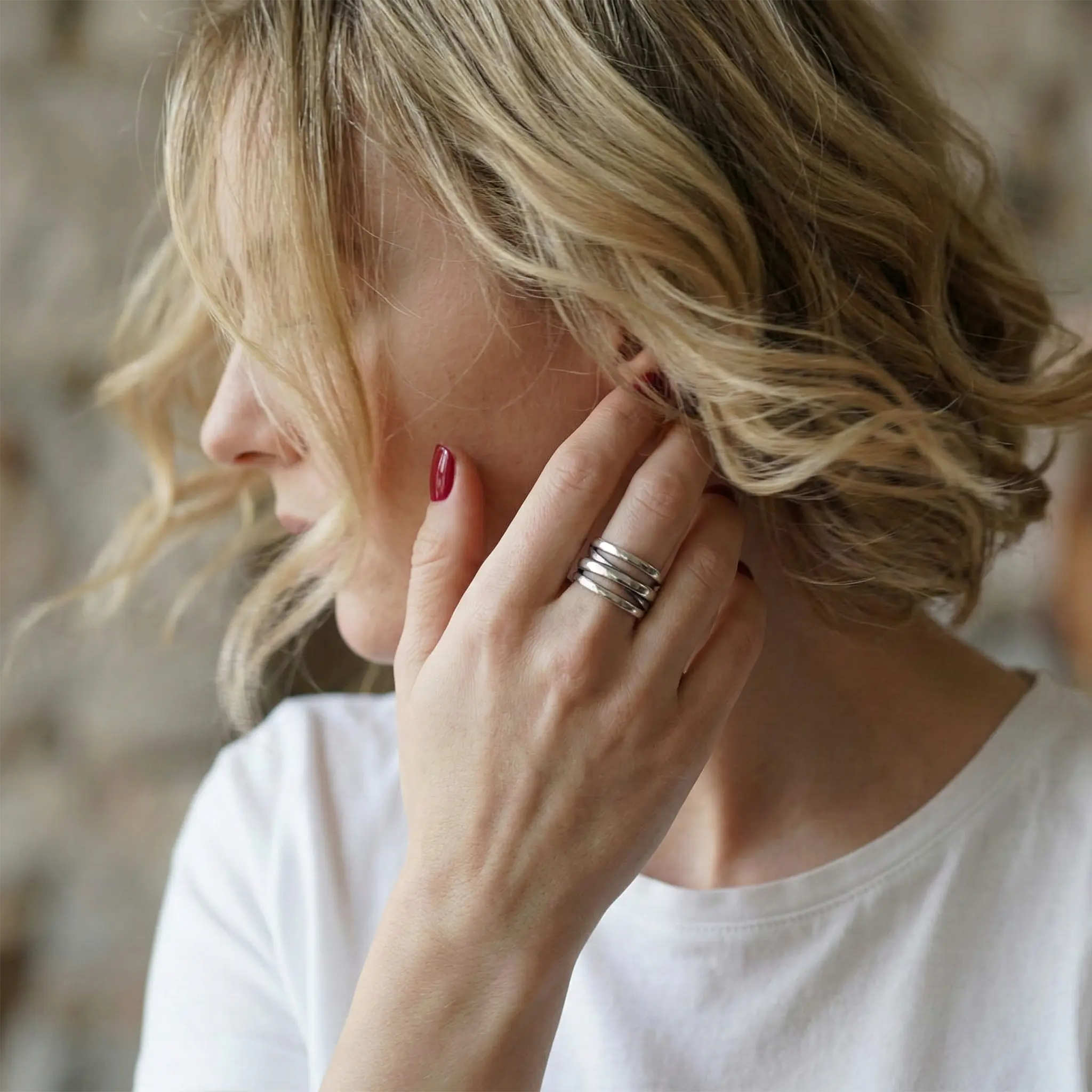 Detaillierte Ansicht der Hände einer blonde Frau mit glänzendem, tiefrotem Nagellack, die auf Denim-Stoff verschränkt sind. Am Mittelfinger trägt sie den markanten, breiten Sterling-Silber-Wickelring im Vintage-Look.