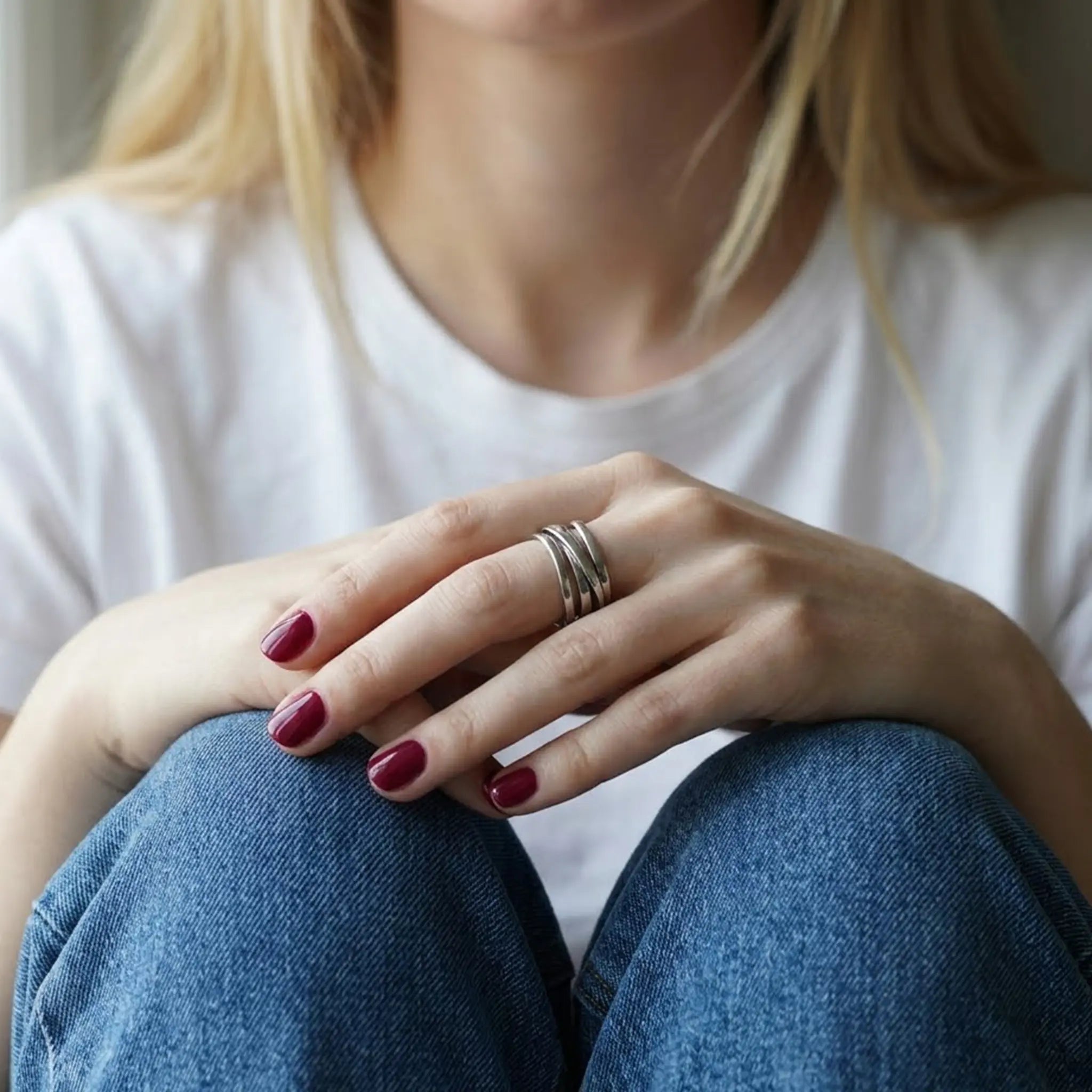 Nahaufnahme einer Hand mit dunkelrotem Nagellack auf blauem Denim, die einen breiten, verstellbaren Wickelring aus 925er Silber trägt.