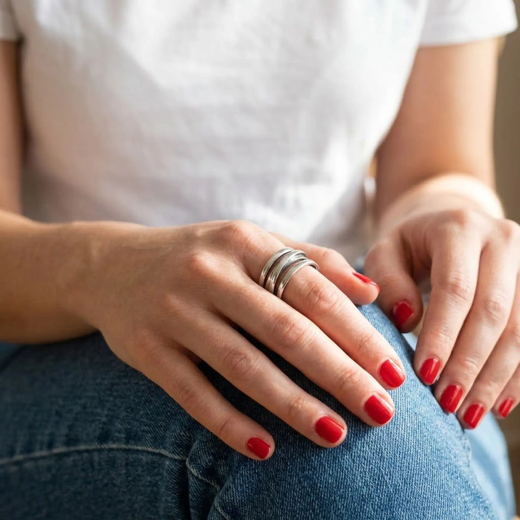 Detailaufnahme eines breiten Silberrings 925 verstellbar an einer Frauenhand mit dunkelrotem Nagellack, moderner Wickelring aus echtem Silber im Boho-Stil vor Jeans-Hintergrund.