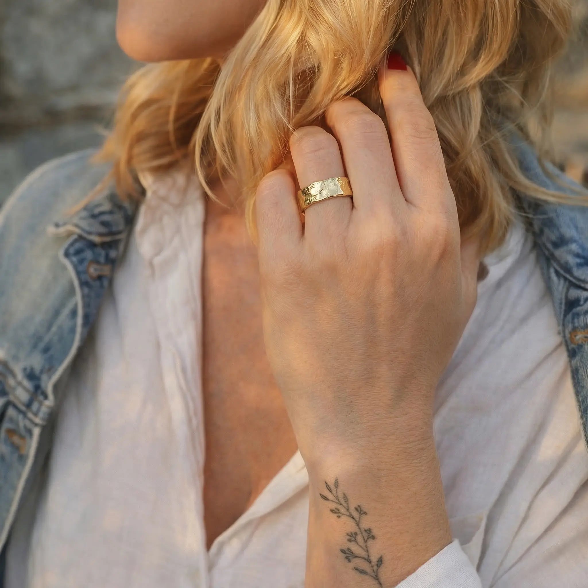 Goldener Damenring aus 925 Sterling Silber vergoldet, moderner breiter Ring mit gehämmerter Struktur, getragen an der Hand einer Frau mit Jeansjacke und botanischem Tattoo