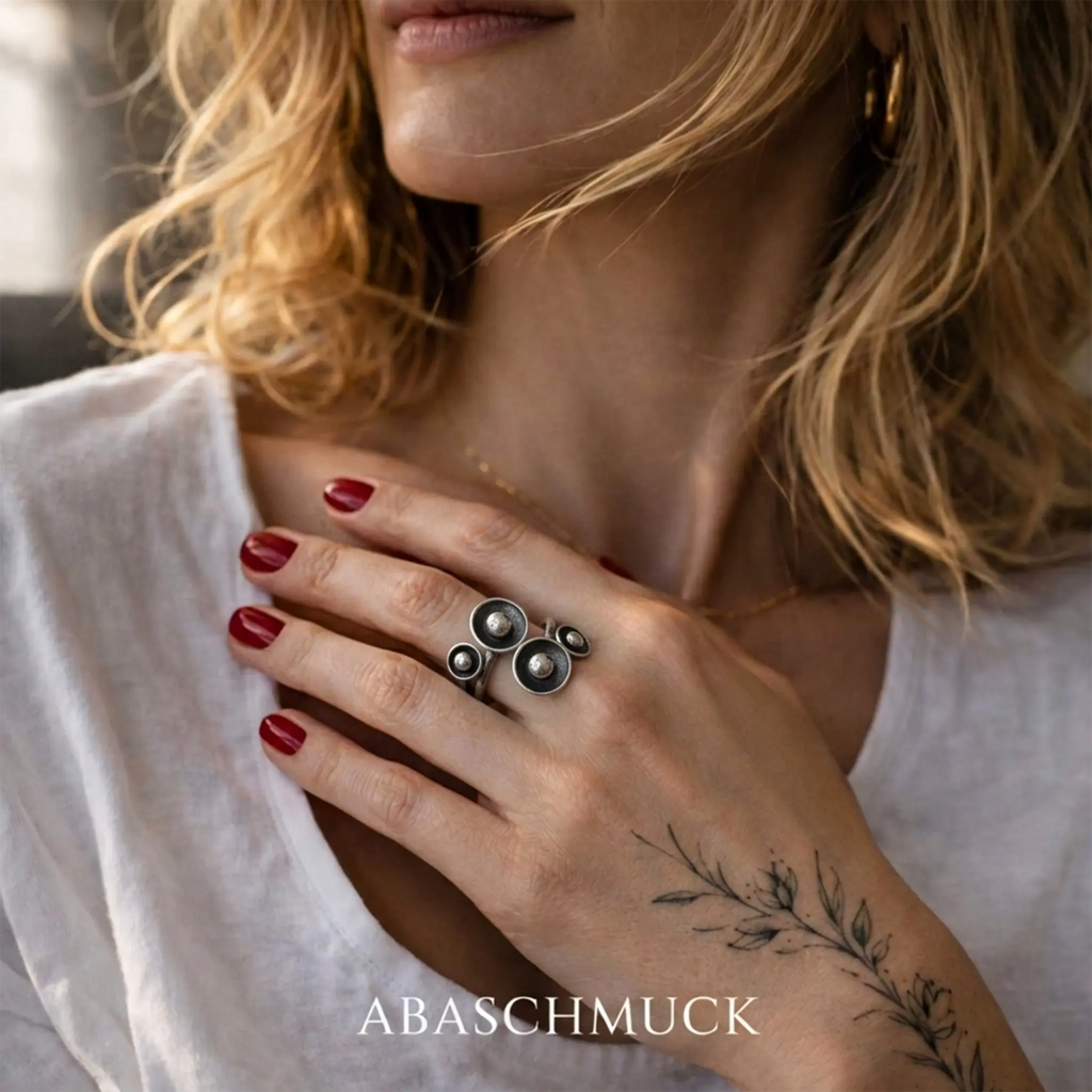 Großer Silberring 925 für Damen mit modernem Kugeldesign, auffälliger Statement Ring an der Hand einer blonden Frau mit weißer Bluse, rotem Nagellack und botanischem Tattoo