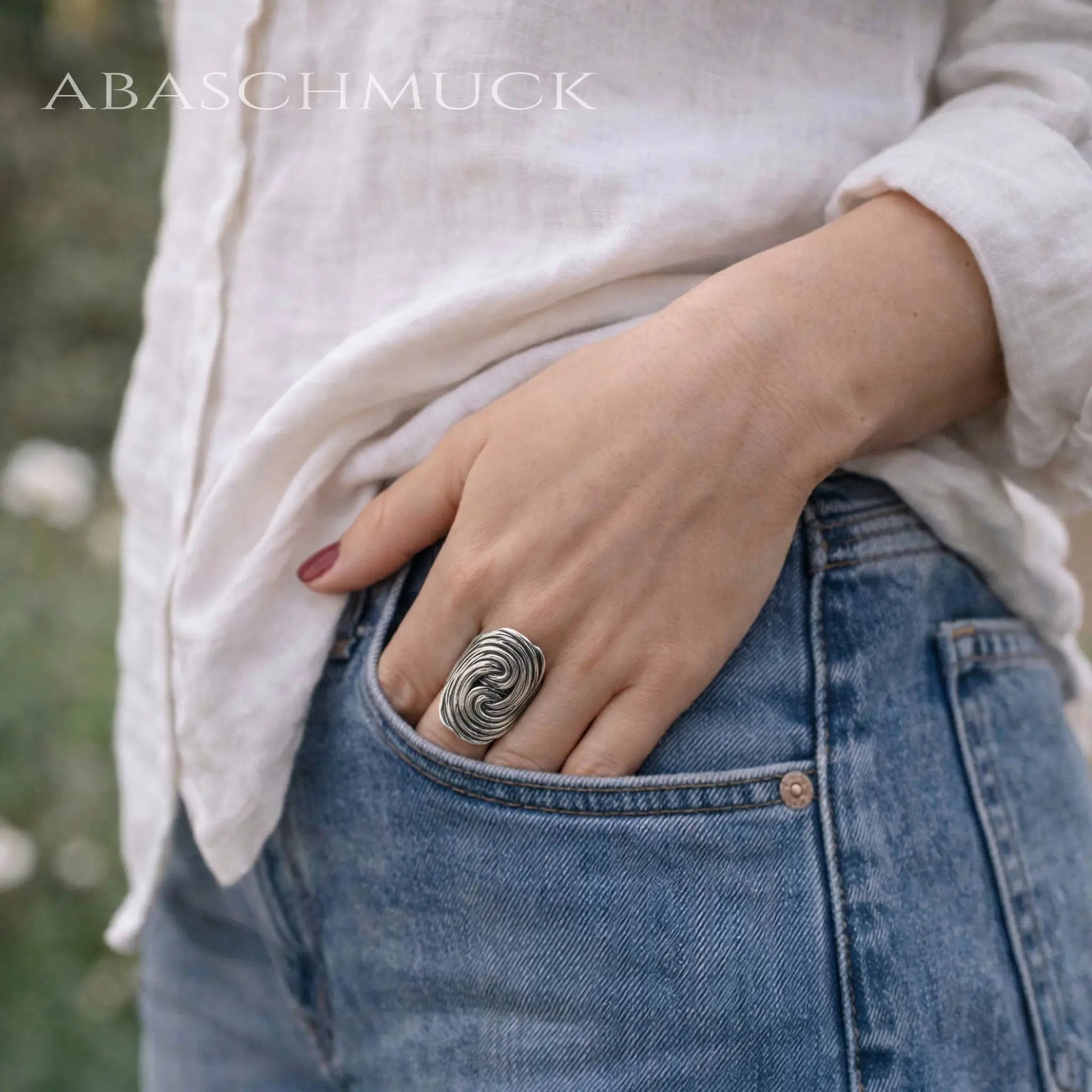 Hand in der Jeans-Tasche zeigt den großen Sterling Silber Ring im Kontrast zum blauen Denim-Stoff.