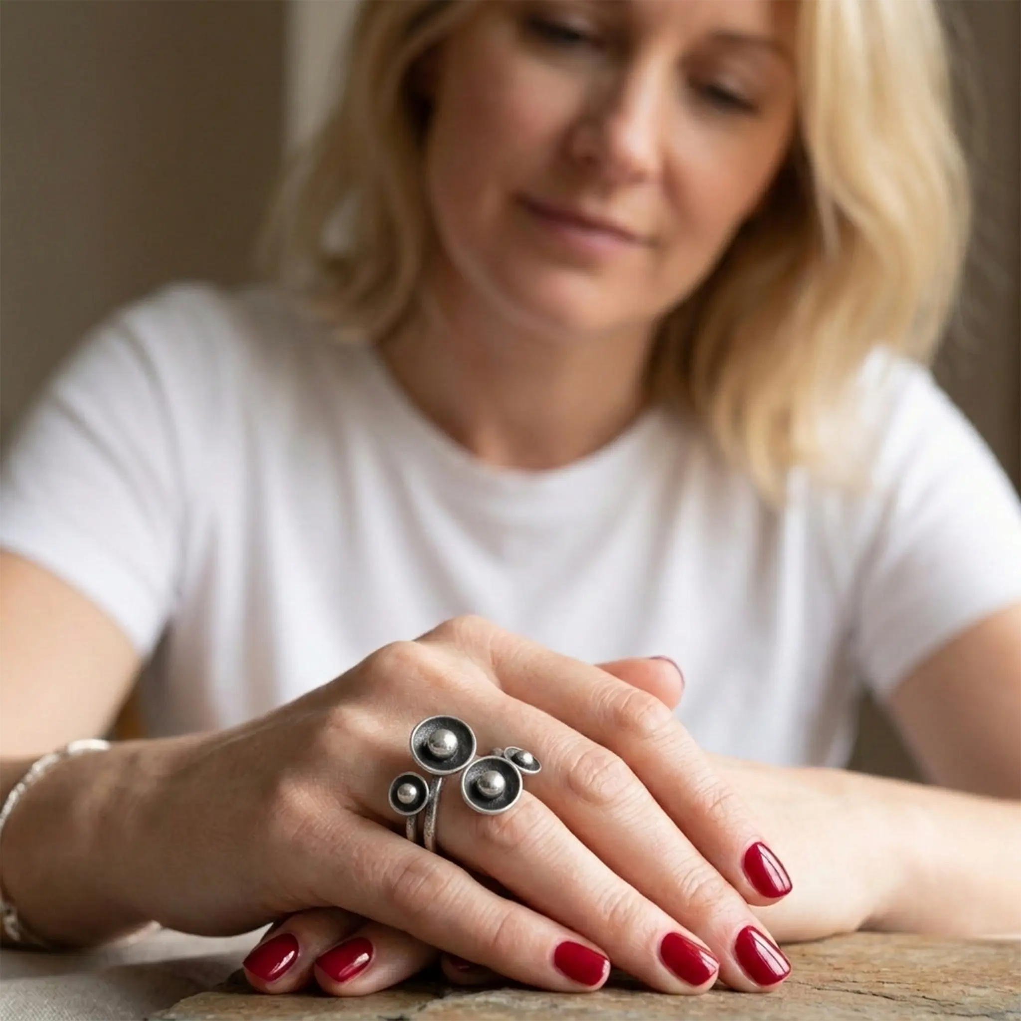 Verstellbarer Silberring aus 925 Sterling Silber mit kreativem Kugelmotiv, moderner Damenring an der Hand einer blonden Frau im natürlichen Lifestyle Look auf rustikalem Holztisch