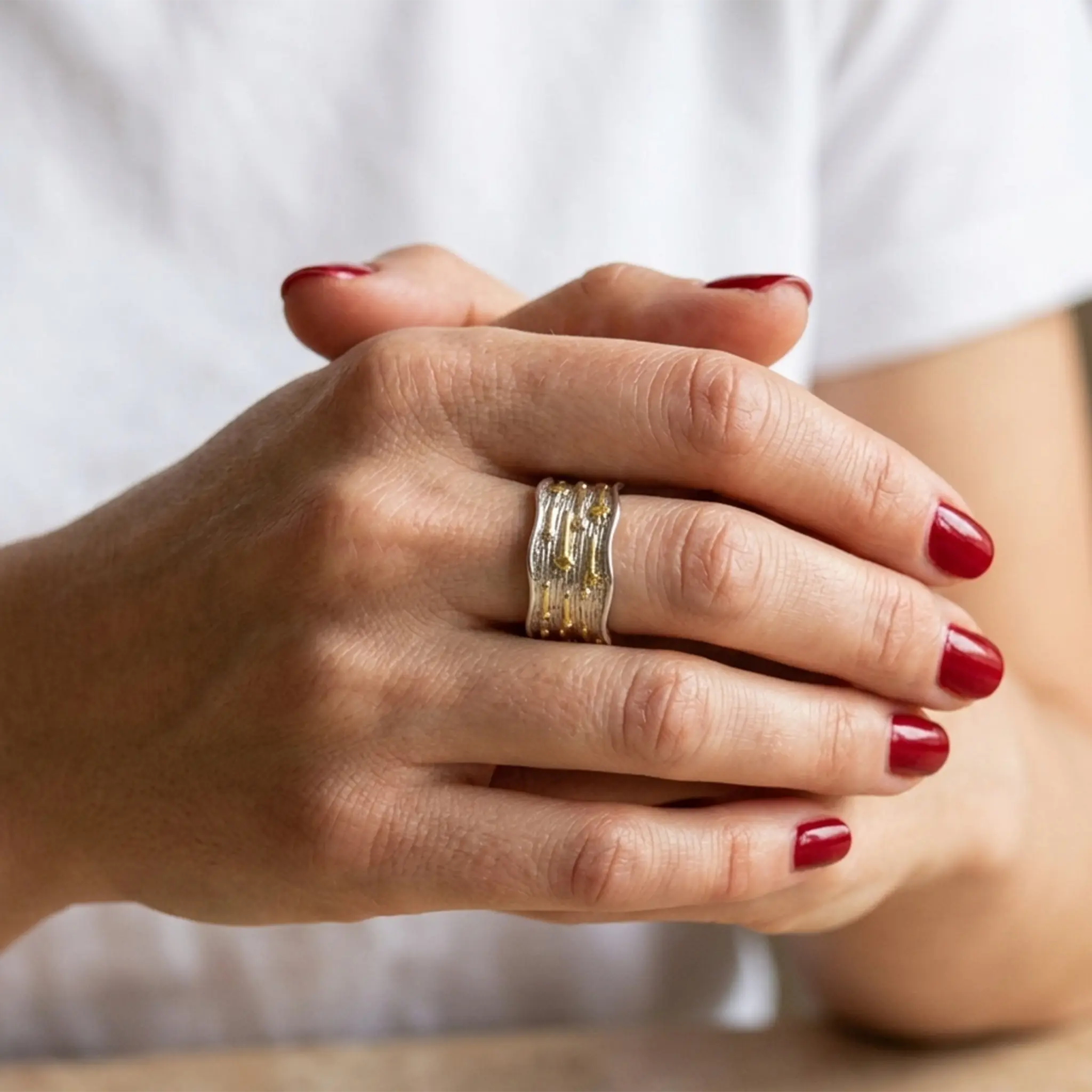 Breiter Statement-Ring aus 925 Silber mit Gold-Akzenten an gefalteten Händen.
