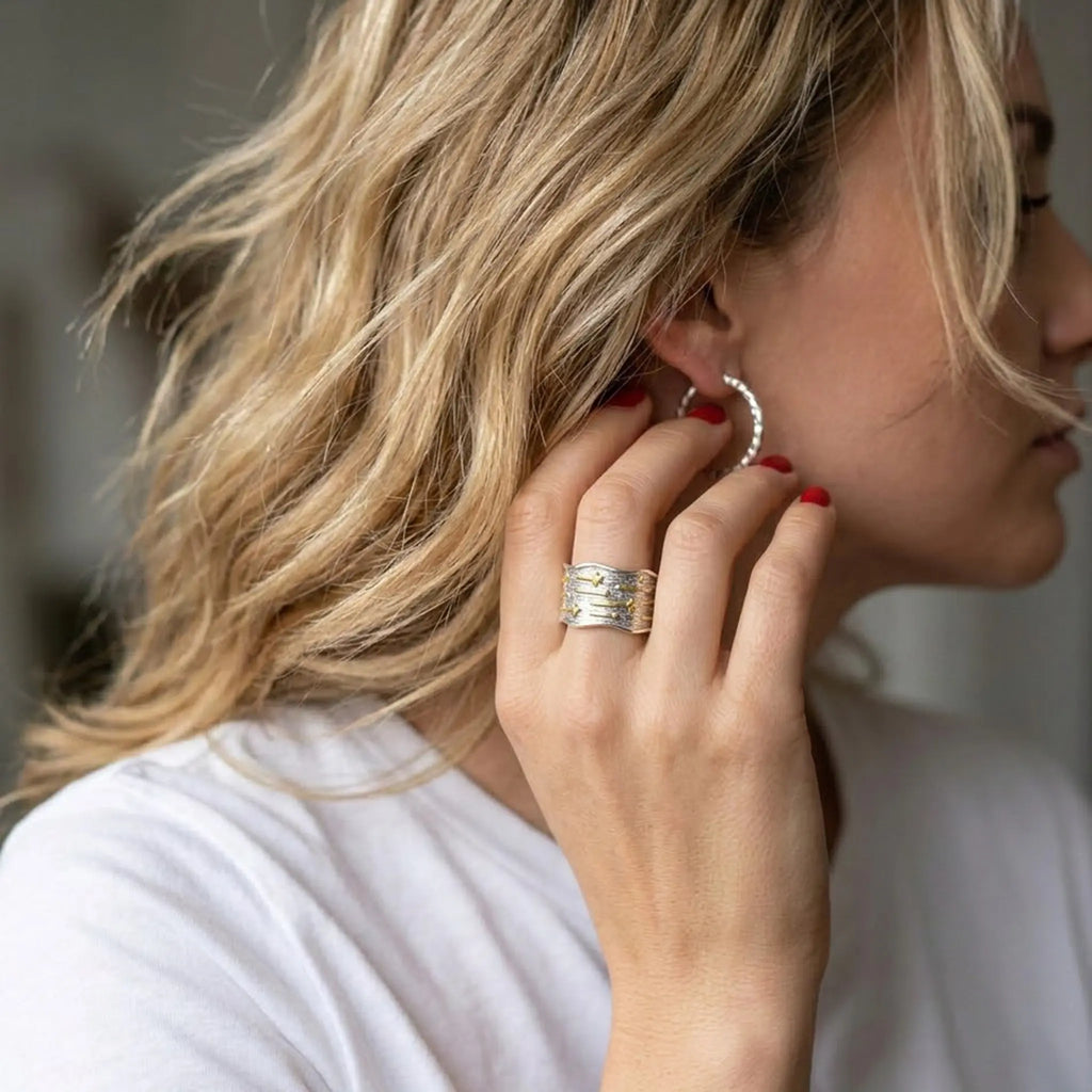 Massiver Silberring mit Gold-Details getragen von Frau mit Creolen – Lifestyle-Schmuck.