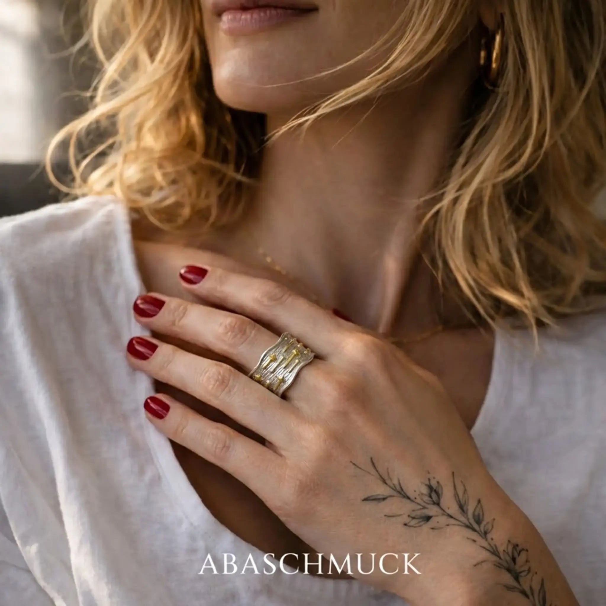 Abaschmuck Bicolor Ring Damen breit und gewellt – Nahaufnahme mit floralem Tattoo.