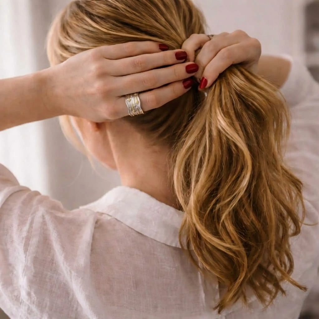 Rückansicht: Frau mit blondem Haar und breitem Silber-Gold-Ring am Finger.