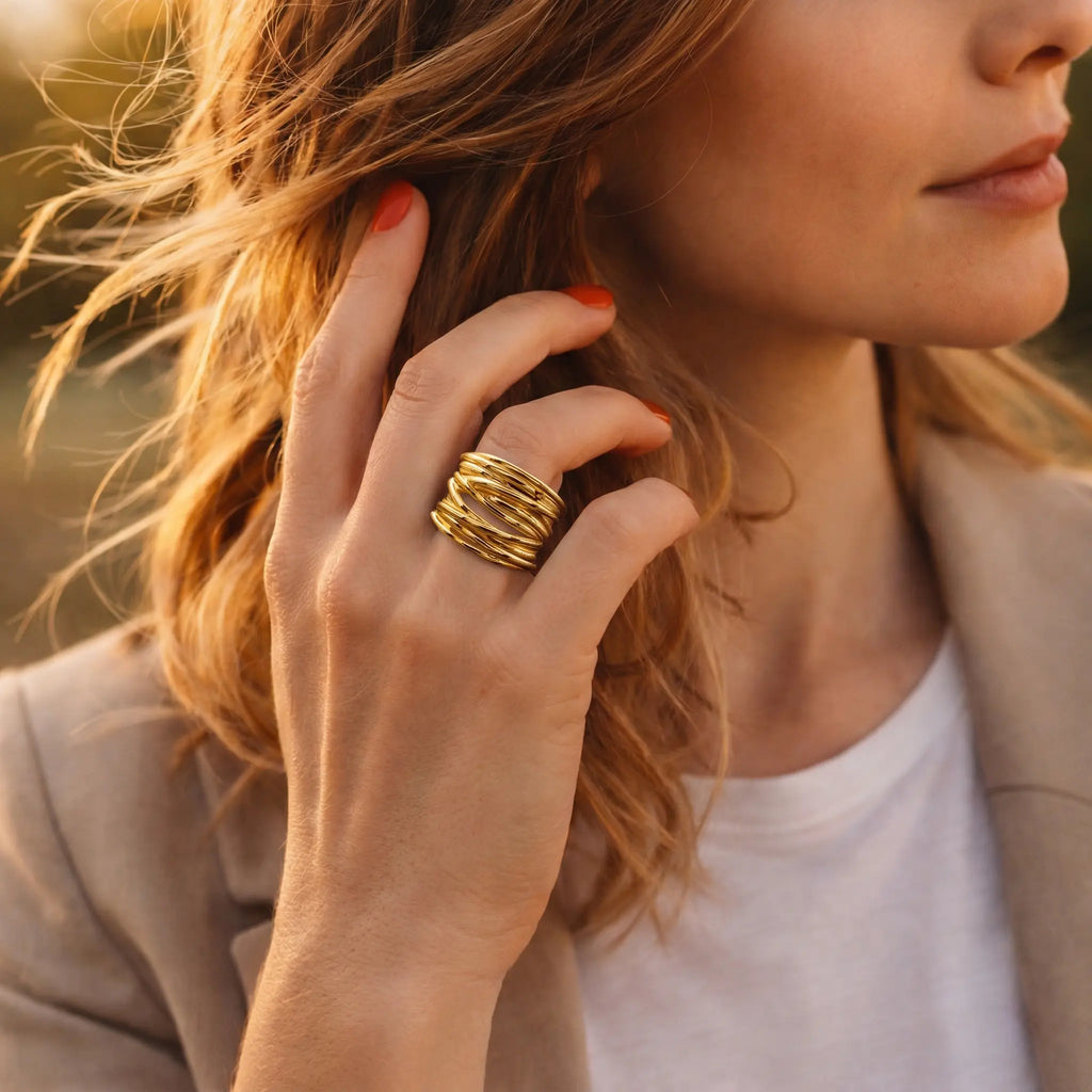 Vergoldeter Damenring aus 925 Sterling Silber mit modernem geschwungenem Design, stilvoller Statement Ring an der Hand einer Frau mit beigem Blazer im goldenen Sonnenlicht
