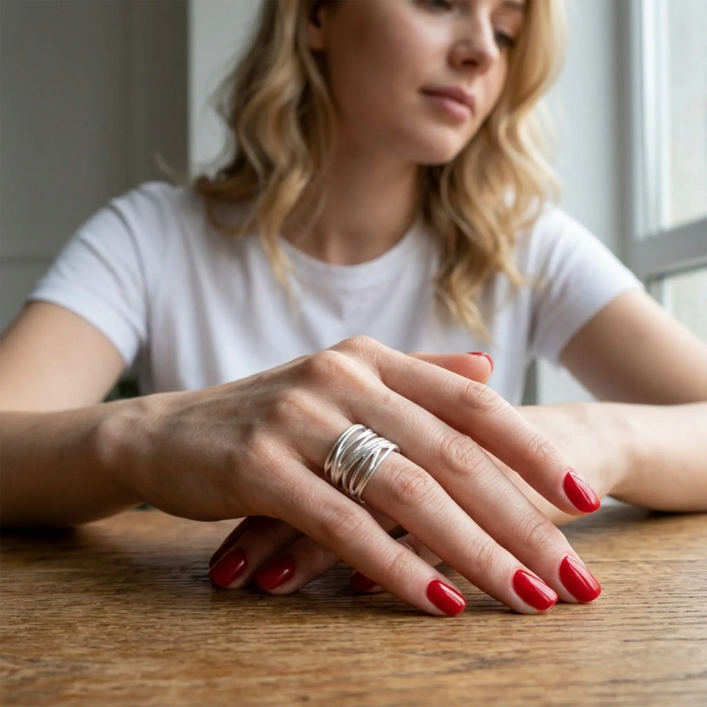 Frau mit roten Nägeln trägt verstellbaren Silberring 925 Bandring offen am Finger – natürlicher Look am Holztisch