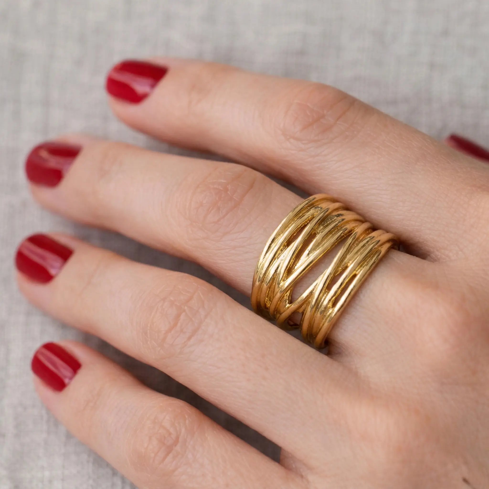 Breiter vergoldeter Silberring 925 für Damen, moderner mehrlagiger Ring mit glänzender Oberfläche, detailreiche Nahaufnahme an der Hand mit rotem Nagellack