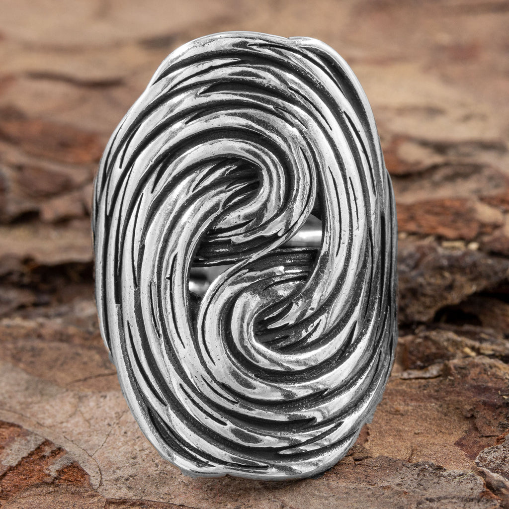 Frontalansicht des verstellbaren Silberrings, die das kunstvolle, ovale Design und die detaillierte Goldschmiedekunst der fließenden Linien auf Naturhintergrund zeigt.
