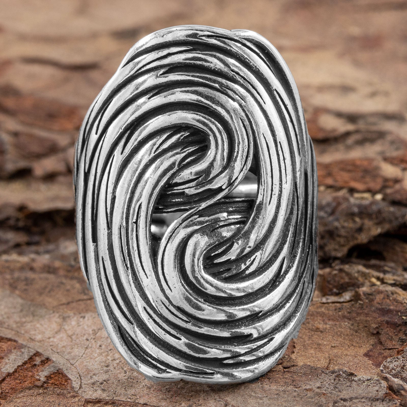 Frontalansicht des verstellbaren Silberrings, die das kunstvolle, ovale Design und die detaillierte Goldschmiedekunst der fließenden Linien auf Naturhintergrund zeigt.