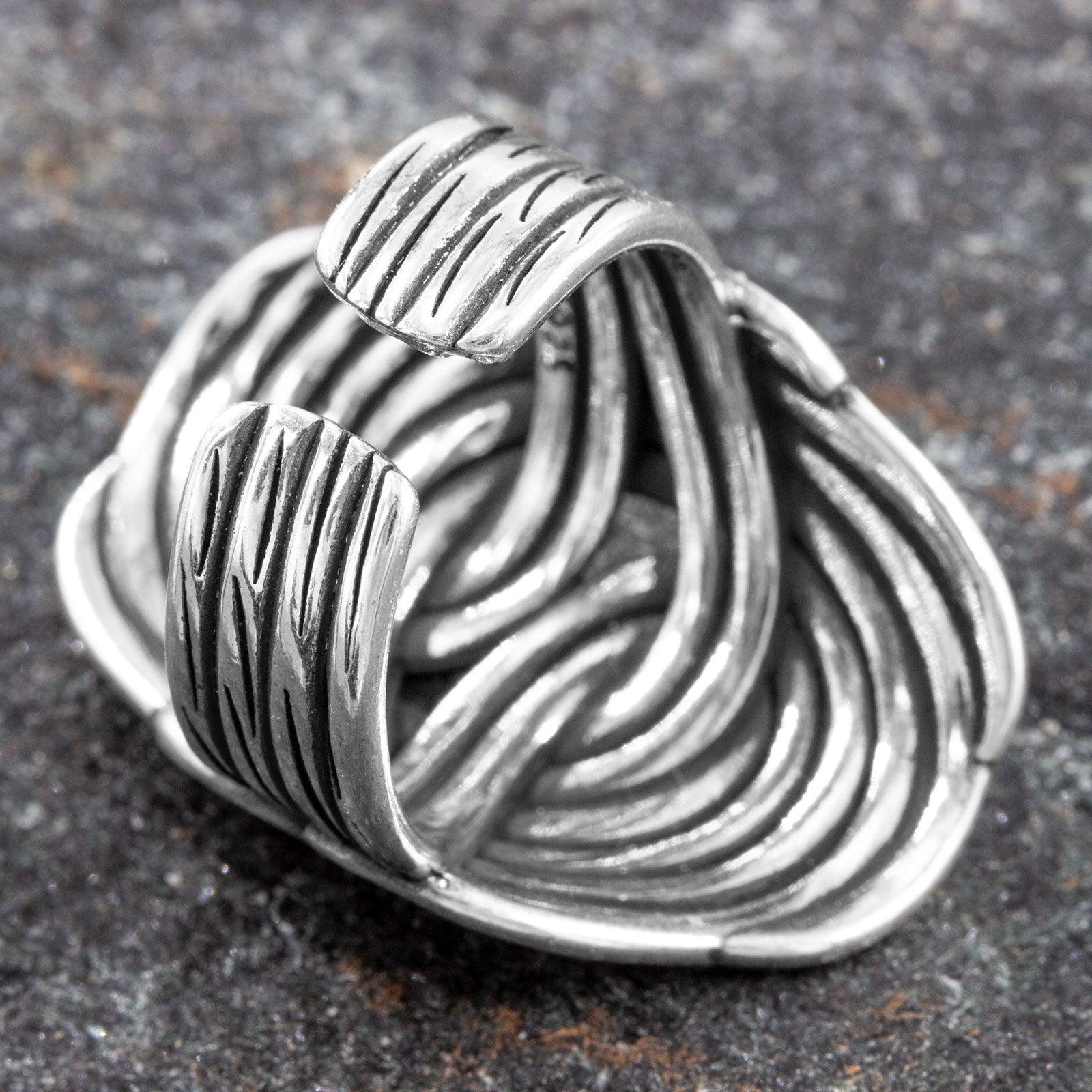 Perspektivische Ansicht von oben auf dunklem Stein, die das Spiel der geschwungenen Silberstränge und die solide Bauweise des Bandrings zeigt.