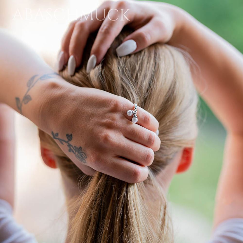 Ring mit Perlenanhängern am Finger einer Frau, Hände im Haar.