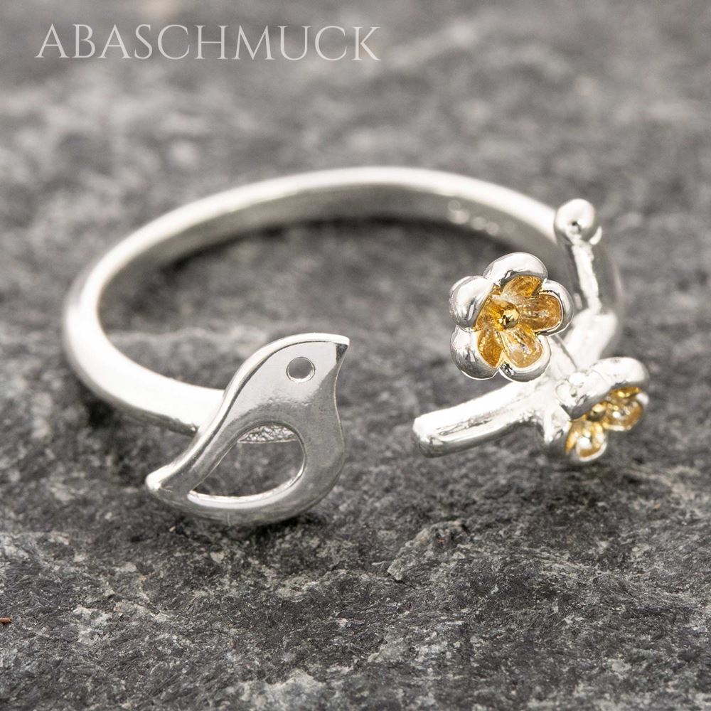 Zarter offener 925er Silberring mit Vogel und zwei kleinen goldenen Blüten in leicht seitlicher Ansicht.