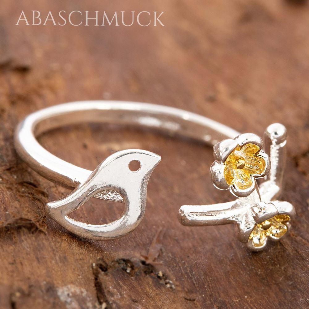 Silberring mit Vogelmotiv und goldfarbenen Blüten auf Holzoberfläche fotografiert.