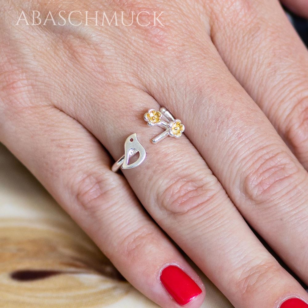 Ring an einer Hand getragen, Vogel und goldene Blüten deutlich sichtbar, dezenter femininer Look.