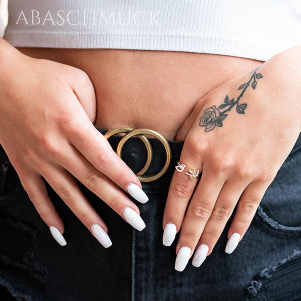 Getragener Silberring mit Vogel und Blüten an beiden Händen vor Jeansbund, moderner und verspielter Stil.