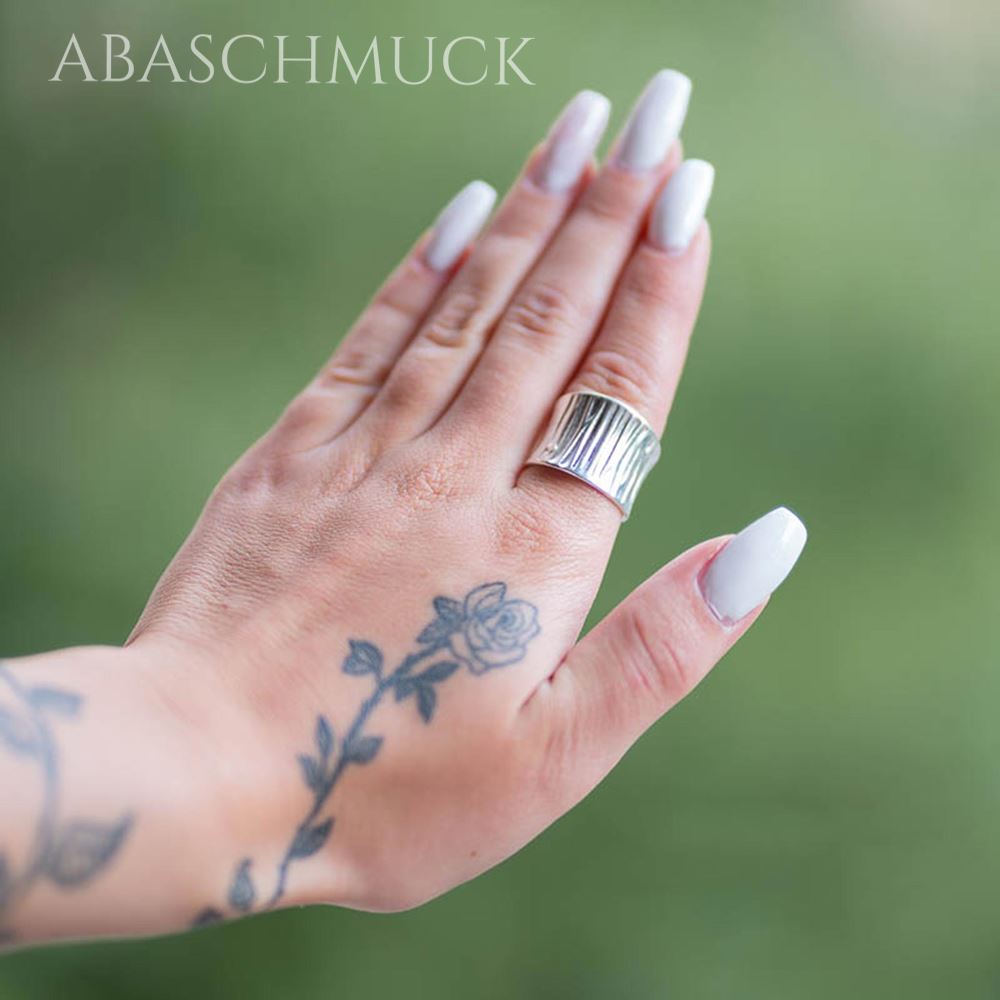 Handaufnahme mit breitem strukturiertem Silberring, weiß lackierte Nägel.