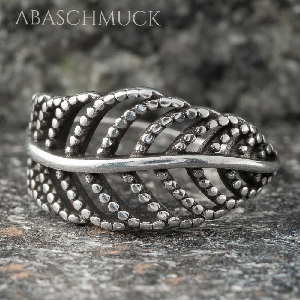 Silberner Bandring im filigranen Blattmuster auf dunkler Steinoberfläche.