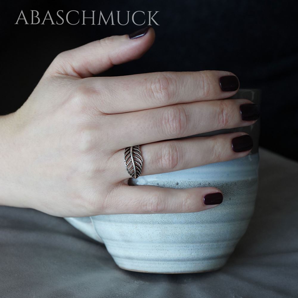 Damenhand mit dunkel lackierten Nägeln trägt filigranen Blattdesign-Silberring.
