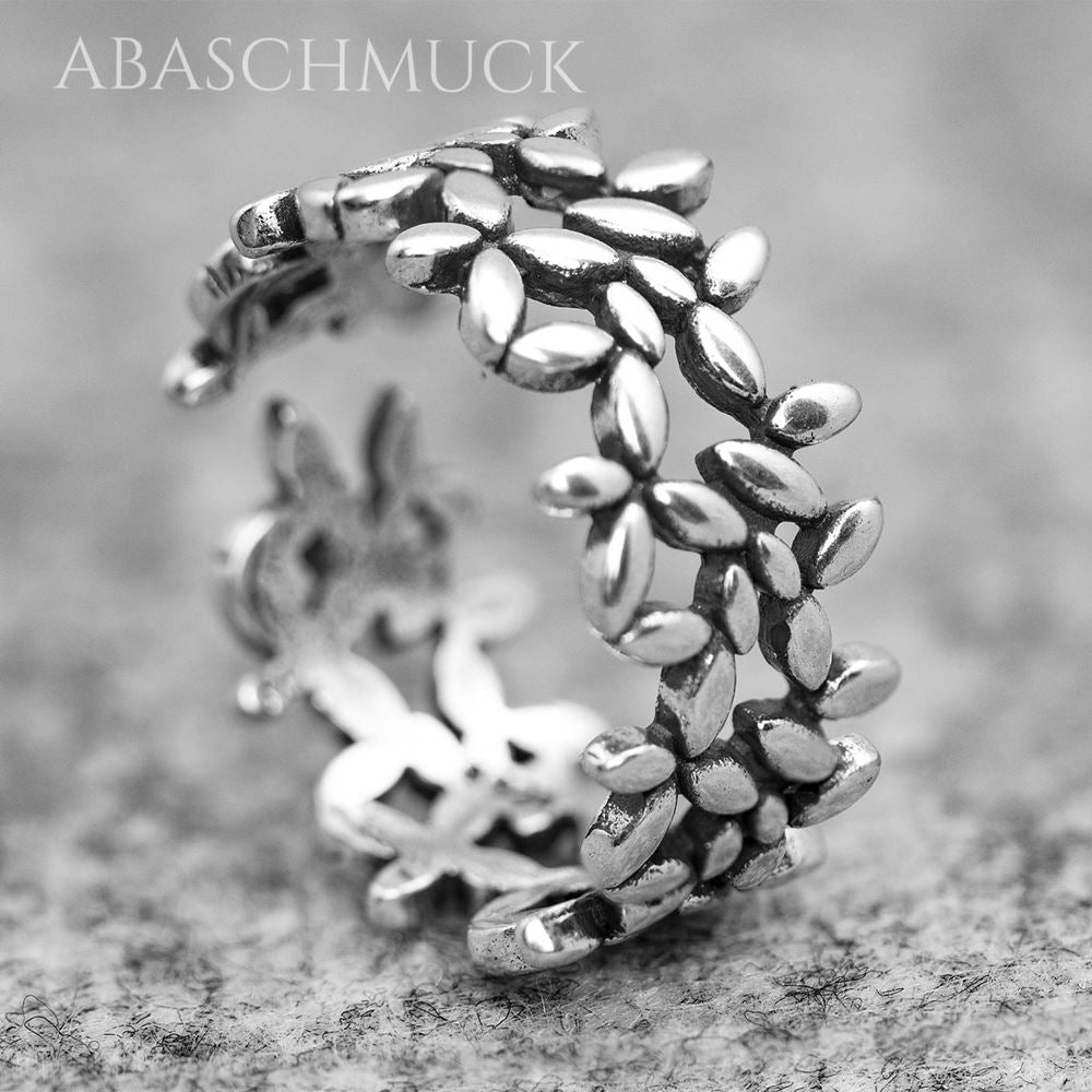 Runder, offener Silberring mit filigranem Blätterdesign, aufgenommen auf einer hellgrauen strukturierten Fläche.