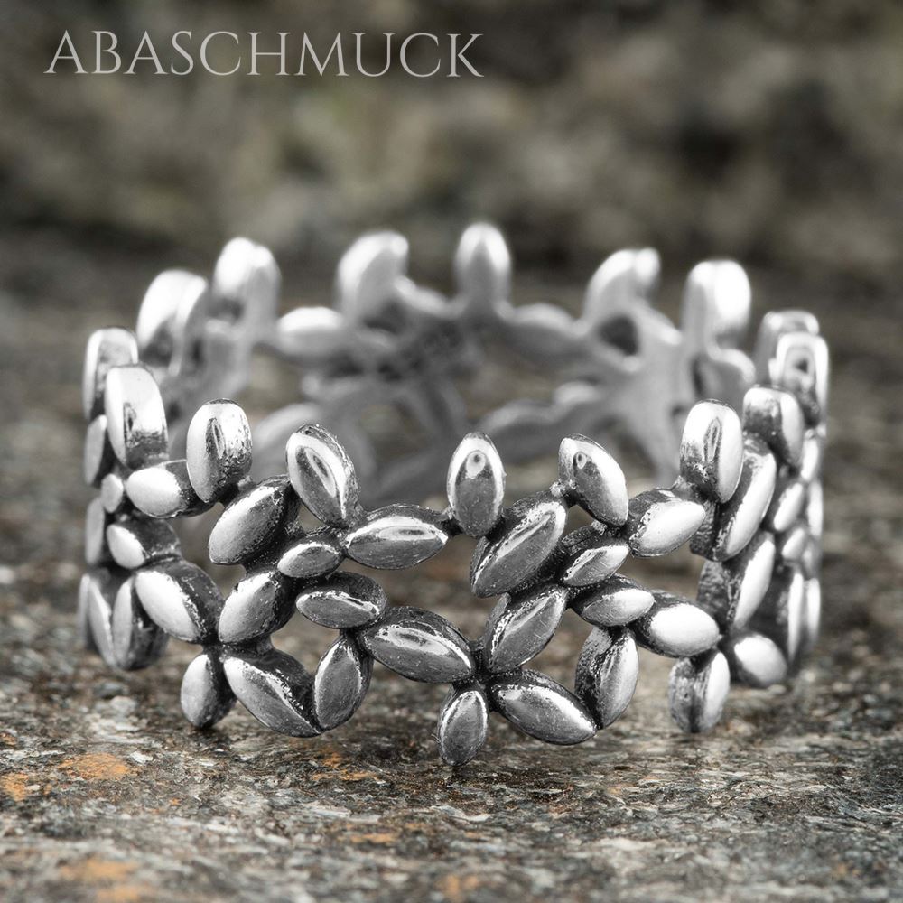 Floraler Silberring mit glänzenden Blättchen, stehend auf einer strukturierten Steinoberfläche.