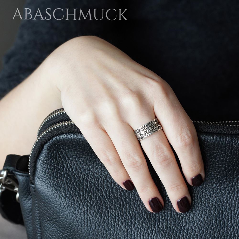 Hand mit breitem ornamentiertem Silberring liegt auf einer schwarzen Lederhandtasche.