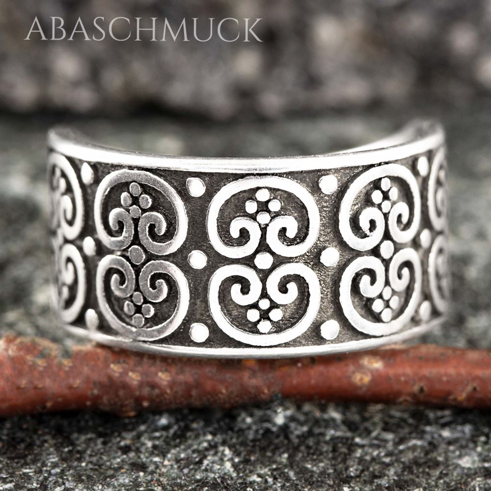 Nahaufnahme eines breiten offenen Silberrings mit kunstvollem Ornamentmuster auf Steinfläche.