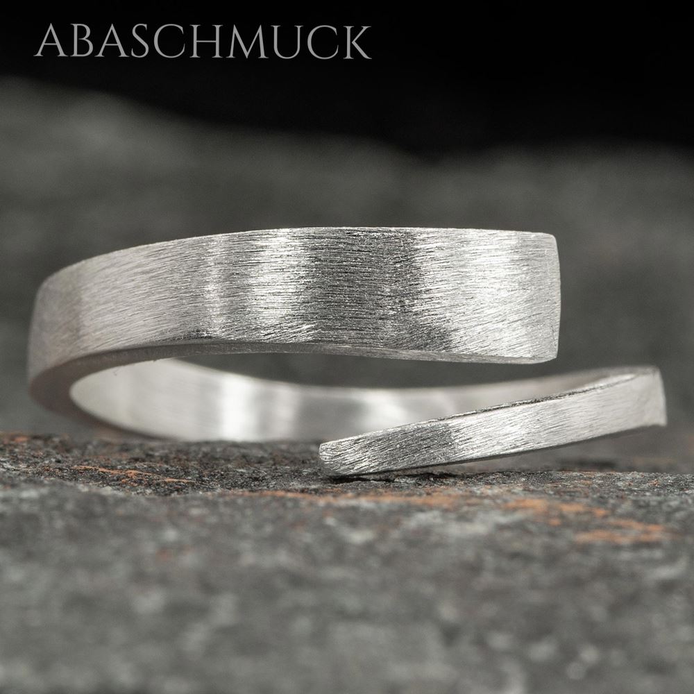 Offener gebürsteter Silberring liegt auf einer Steinoberfläche.