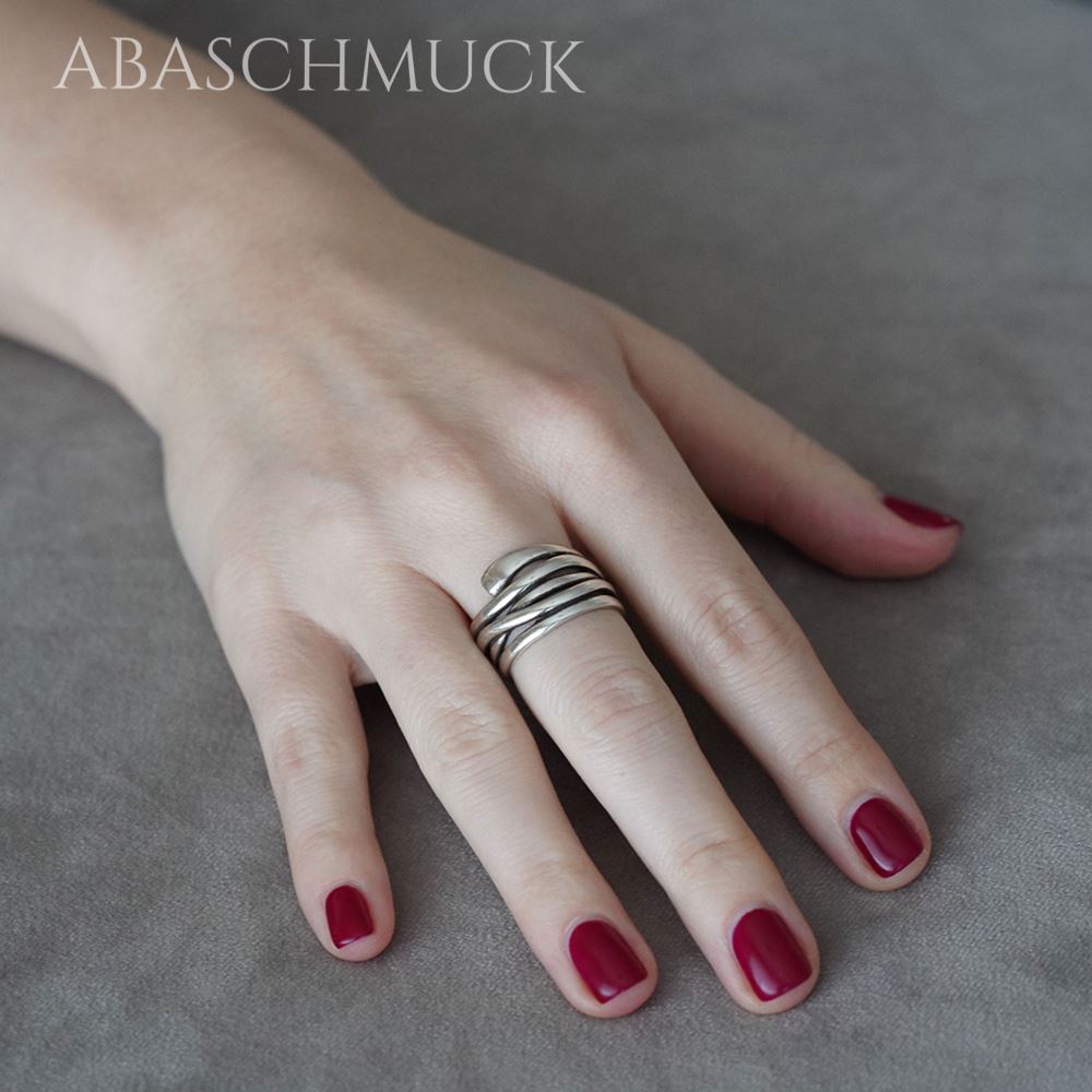 Hand mit dunkelrotem Nagellack trägt einen breiten geschwungenen Silberring.
