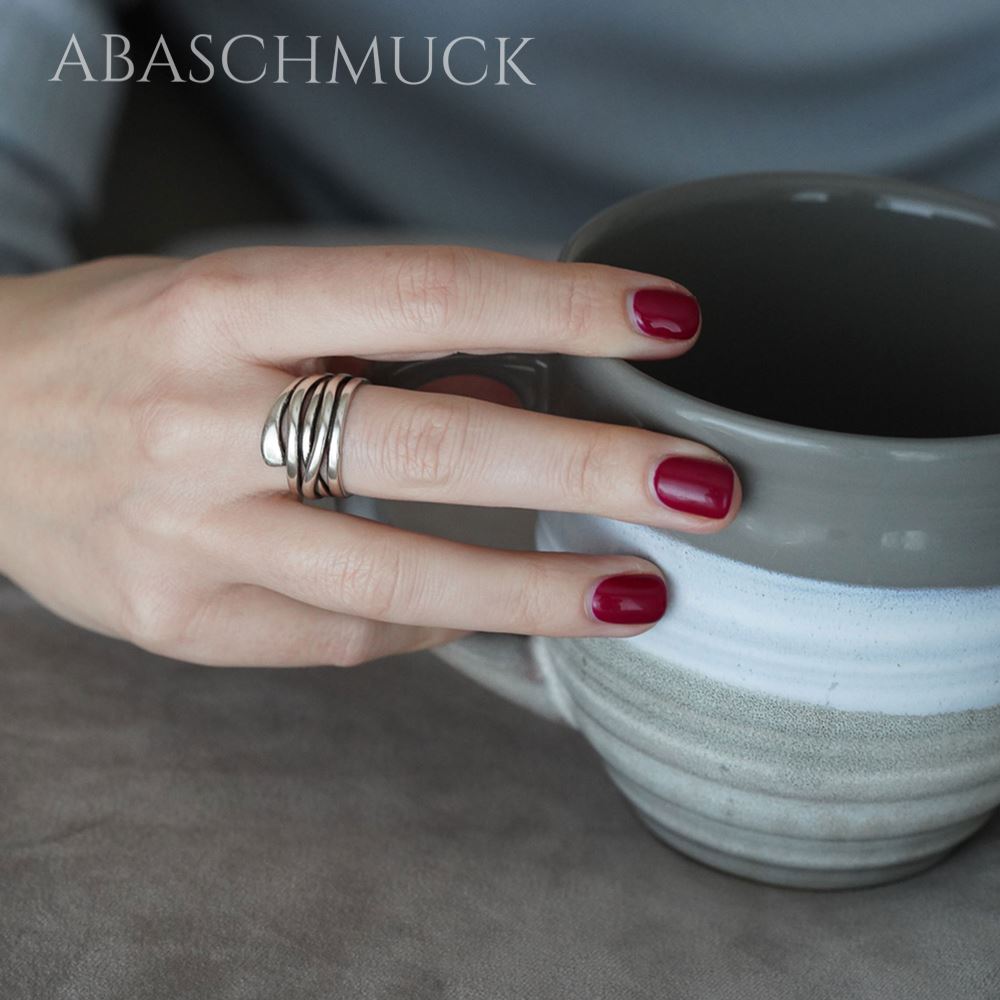 Hand mit breitem offenem Silberring hält eine graue Keramiktasse.
