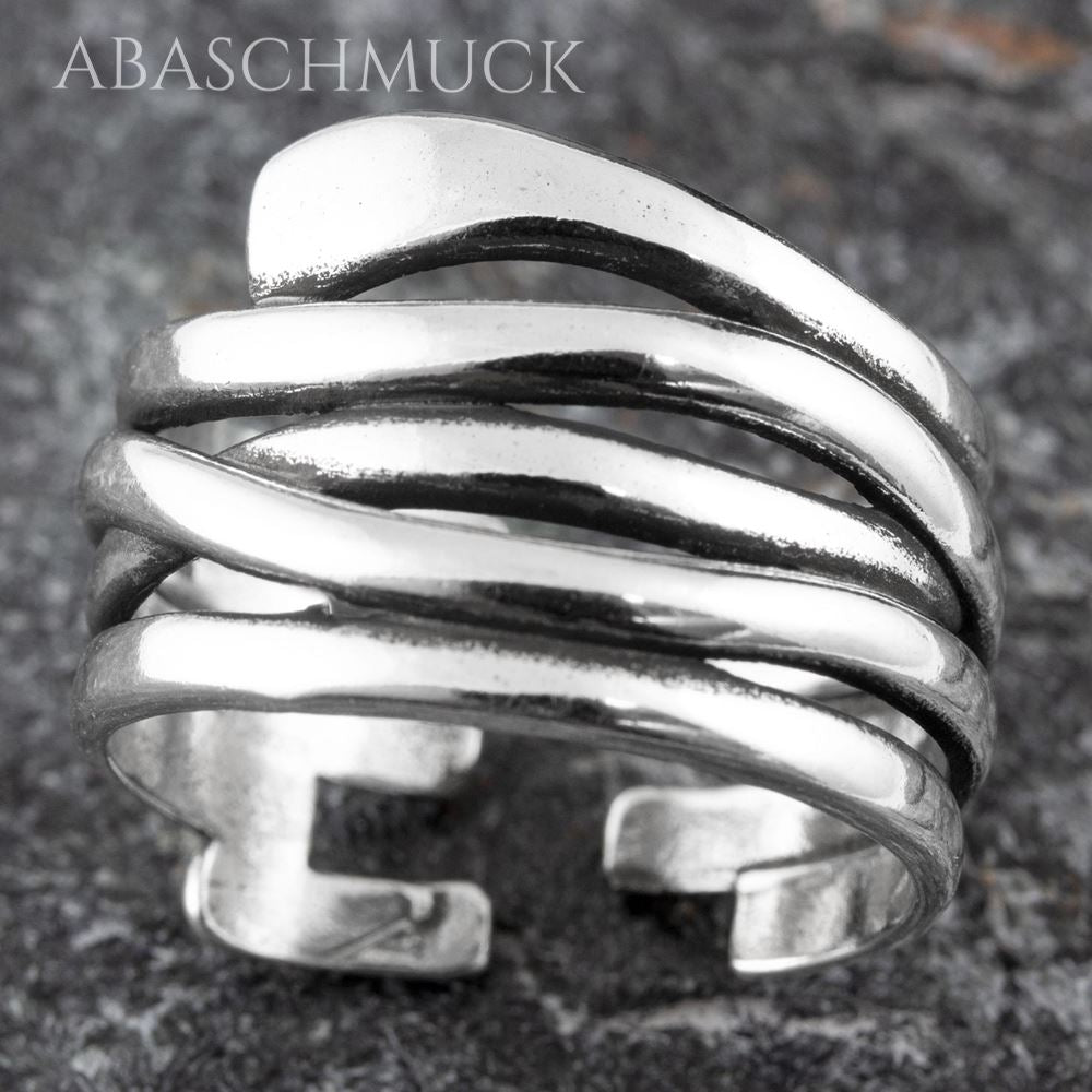 Nahaufnahme eines breiten offenen Silberrings mit geschwungenem Mehrband-Design auf Stein.