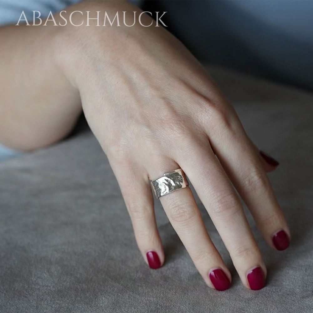 Hand mit rotem Nagellack trägt breiten strukturierten Silberring.