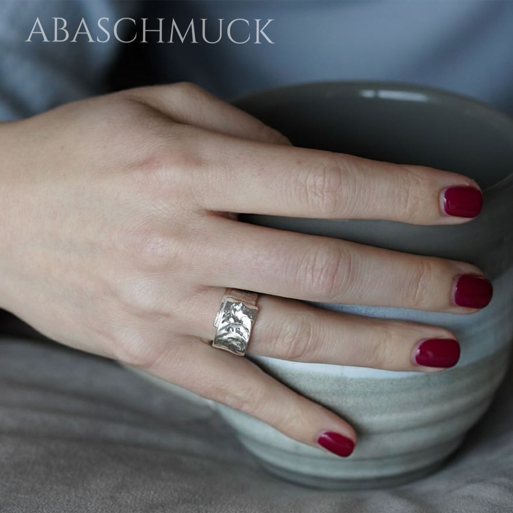 Hand mit strukturiertem Silberring hält eine graue Keramiktasse.