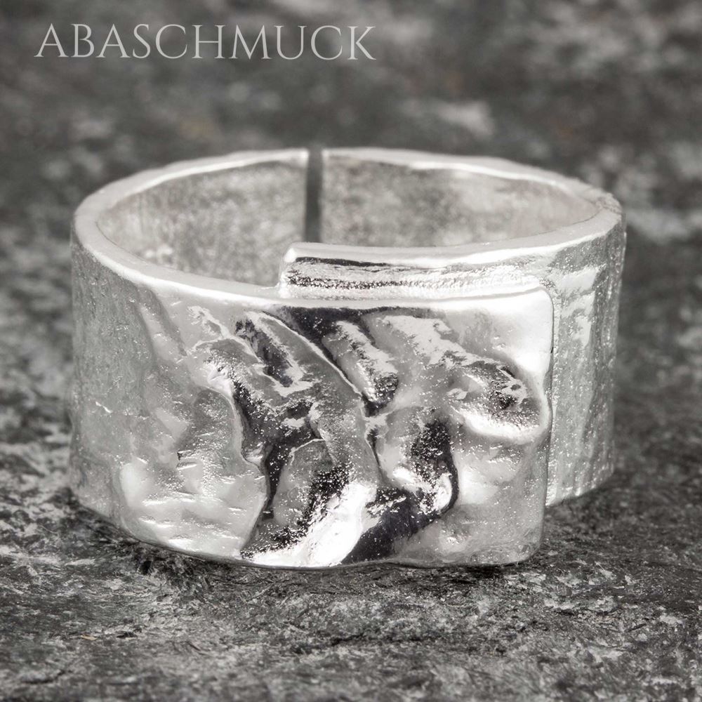 Nahaufnahme eines breiten strukturierten offenen Silberrings auf Steinoberfläche.