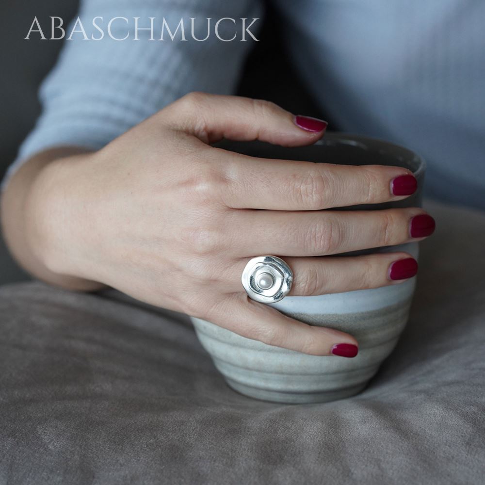 Damenhand mit Perlen-Blumenring beim Halten einer Tasse