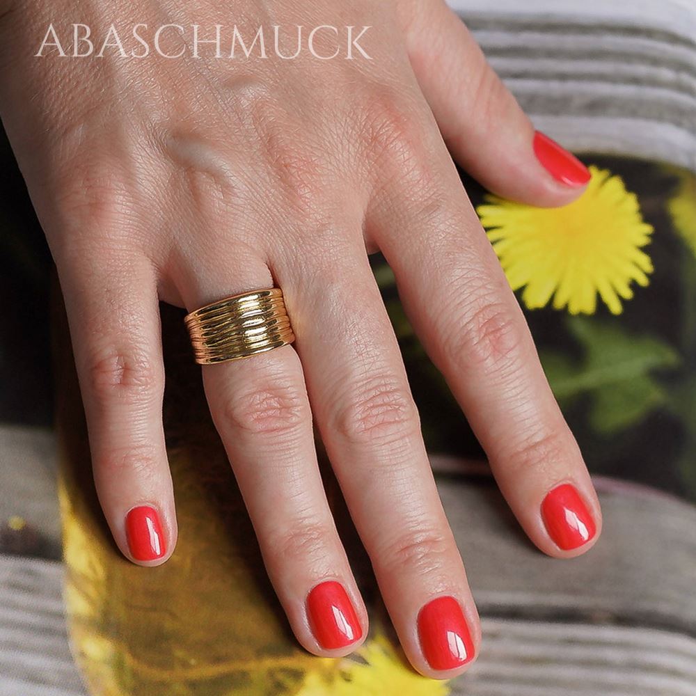 Breiter goldfarbener Ring im Wellen-Design an einer Hand im Tageslicht.
